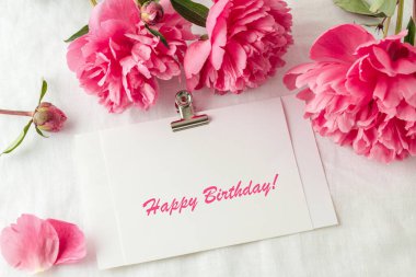 Şakayık çiçekleri ve saf keten masa örtüsü arka planında Mutlu Yıllar kartpostalı. Çiçek kartı, klasik tarzda. Sahte doğum günü tebrik kartı..