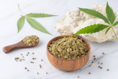 Ahşap kasede kenevir tohumu tozu ve beyaz mermer arka planda kenevir yaprakları. Süper yiyecek olarak kenevir tohumlarından un, lif, protein ve omega 3 ile yemek için destek.