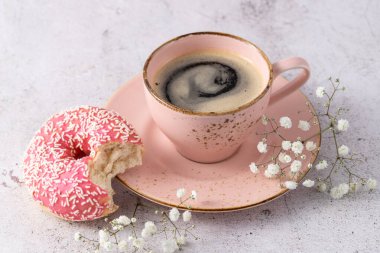 Isırılmış pembe jöleli donut ve taş masaya yakın kahve fincanı. Kahve molasında tatlı olarak taze çörek.