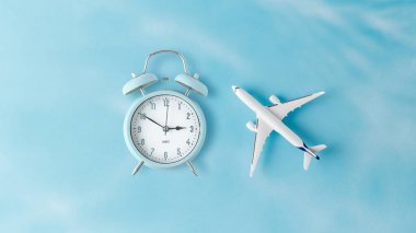 Mavi zemin üzerinde beyaz model uçak ve alarm saati var. Seyahat kavramı.