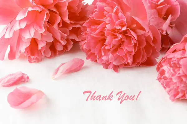 Thank you card. Pink coral peony flowers with falling petals on white linen table cloth background. Bouquet of peonies. Floral card with peony flowers and german word Thank you.