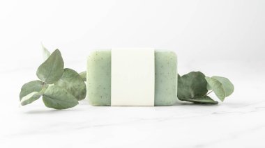 Boş kağıt kapaklı yeşil bitkisel sabun ve beyaz mermer masa zemininde kurumuş okaliptüs dalları. Vücut bakımı el işi ürünü ya da spa sağlık konsepti. Kopyalama alanı olan maket kartı
