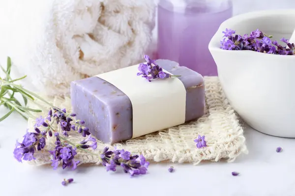 Aroma herbal handcraft soap with lavender flowers for bath relaxation and body care on sisal net bag over white marble table background. Home spa lifestyle.