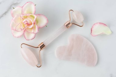Gül kuvars yüz silindiri ve misket masasında pembe gül çiçekli yaşlanma önleyici cilt masajı için gua sha taşı. Yüz masajı için kozmetik araç.