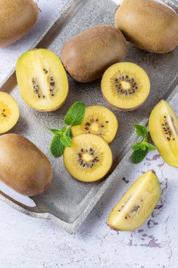 Olgun çiğ kivi bütün olarak ve gümüş metalik tepside dilimler kırsal taş masada nane yaprakları ile. Üst görünüm