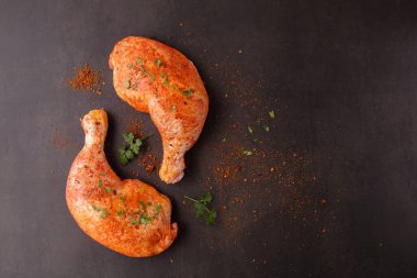 Domates sosunda salamura edilmiş, bitkiler ve kahverengi taş zemin üzerinde pişmemiş tavuk bacakları. Baharatlı tavuk budu pişirmeye ya da ızgara yapmaya hazır. Kopyalama alanı olan mutfak arkaplanı.