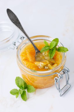 Tatlı narenciye reçeli ya da cam kavanozda beyaz mermer masa zemininde nane yapraklı marmelat. Şekerli kabuklu portakal reçeli. Egzotik turunçgiller tatlı ürünü.