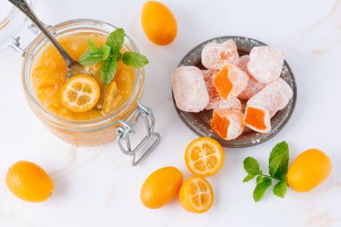 Tatlı kumkatlı reçel ya da cam kavanozda marmelat, doğu usulü lezzetli lokum ve taze çiğ bütün ve beyaz mermer masa arkasında nane yapraklı dilimlenmiş meyve. Egzotik narenciye tatlı ürünleri..