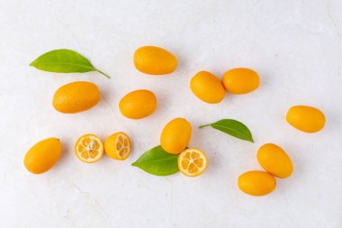 Tatlı ve ekşi kumkat, taze çiğ bütün ve hafif mermer masa arkasında yaprakları olan dilimlenmiş narenciye meyveleri. Egzotik tropik kimyon meyvesi. Üst görünüm.