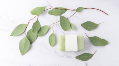 Boş kağıt kapaklı yeşil bitkisel sabun ve beyaz mermer masa zemininde taze kokulu okaliptüs dalları. Vücut bakımı ya da spa sağlık konsepti. Kopyalama alanı olan üst görünüm kartı