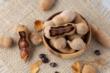 Olgun ve kabuklu demirhindi meyveleri. Ahşap kasede tohumlarla. Kenevir arka planda yakın plan. Sağlıklı egzotik yiyecekler.