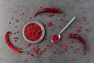 Eski metalik plaka ve kırmızı biberli kaşık üzerinde pembe kuru biber biberi ve gri taş masa zemininde kırıntılar. Aromatik baharatlı mutfak malzemesi. Baharat kartı.