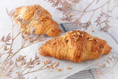 Taze pişmiş fındık kruvasanı beyaz kağıt üzerinde yakın plan ve kurumuş çiçekler retro metal pişirme rafında grunge stone masa arkasında.. 