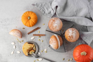 Taze pişmiş balkabaklı tarçınlı kek şekerli pudra üstten sonbahar tatlısı olarak görünüyor. Rafta tatlı kekler, balkabağı sebzeleri ve açık gri taş masa zemininde keten peçeteli tohumlar..