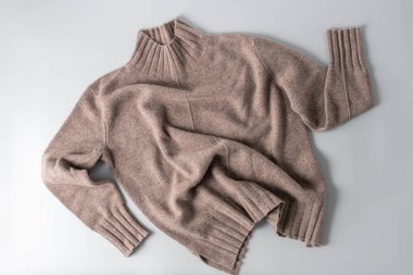 Açık gri arka planda duran, taupe lüks kaşmir yününden yumuşak bir süveter. Sonbahar ve kış saf yün giysiler. Örgü giyim modası..