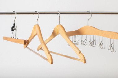 Boş ahşap elbise askıları grubu, metalik korkuluklara, beyaz duvar arkasına yakın çekim yapıyor. Ev ve mağaza aksesuarları.