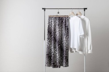 Pamuk gömlekli, beyaz leopar desenli etek ve arka plandaki duvara asılı eşofman üstü. Kadın kıyafetleri içinde moda hayvan baskısı..