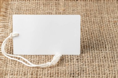 Çuval bezinde ip olan beyaz, boş bir kağıt kart. Kopyalama alanı olan boş etiket.