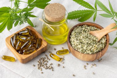 Kenevir tohumu ve yağ süper yiyecekler, lif ve omega 3 ile yemek için takviye. Ahşap kasede ezilmiş kenevir tohumları ve kenevir kumaşında kaşık ve yağ kapsülleri. Kenevir ürünleri konsepti.