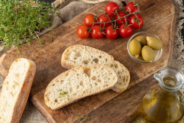 İtalyan ciabatta dilimlenmiş buğday ekmeği, şifalı otlar, kiraz domatesleri ve zeytinler ahşap tahtada, keten havlunun üzerinde. Taze pişmiş ciabatta dilimleri üst görüntüyü yakından gösterir.