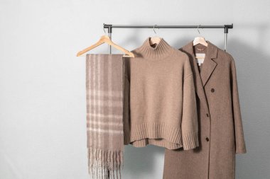 Açık kahverengi yün ceket ya da ceket, bej kaşmir süveter, duvarda asılı alpaka eşarbı. Sonbahar ve kış yün giysileri. Moda monokrom moda.