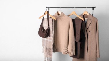 Kahverengi yün ceket ya da ceket, çikolata rengi pantolon, bej kaşmir kazak, alpaka eşarp ve duvardaki askıda duran koyu renk süet çanta. Sıcak yün giysiler. Moda monokrom moda.
