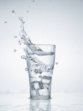 Açık mavi zemin üzerinde cam suya düşen buz küpleri. Sağlıklı içki ve yaşam tarzı.