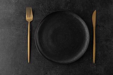 Boş grunge koyu gri el işi seramik tabakta altın çatal bıçak (çatal, bıçak) ve siyah taş kaplama arka plan. Matet bulaşık takımı servis eden Retro tarzı tablo. 