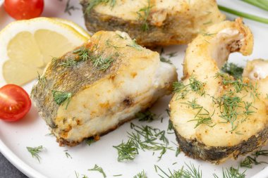 Beyaz seramik tabakta limonlu, dereotlu ve kiraz domatesli fırında zander balığı. Kızarmış tatlı su turna balığı parçaları tabakta..