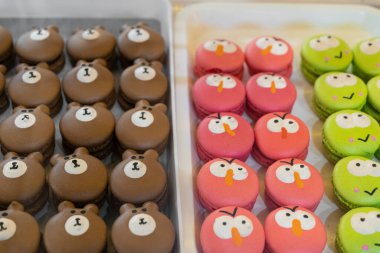 Bu resim renkli karakter temalı makaron tepsilerini gösteriyor, bir çeşit Fransız tatlı krema bazlı şekerleme. Makaronlar sevimli çizgi film suratlarına benzemesi için süslenmiş..