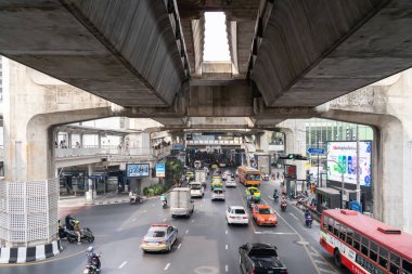 Bangkok, Tayland - 23 Ocak 2025: Kalabalık şehir caddesi, arabalar, taksiler, motosikletler ve beton tren raylarının altında otobüsler. Yoğun trafik ve çeşitlilikle kentsel ulaşım sahnesi