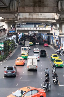 Bangkok, Tayland - 23 Ocak 2025: Kalabalık şehir caddesi, arabalar, taksiler, motosikletler ve beton tren raylarının altında otobüsler. Yoğun trafik ve çeşitlilikle kentsel ulaşım sahnesi