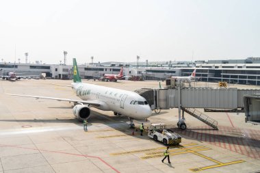 Bangkok, Tayland - 25 Ocak 2025: Havaalanı kapısındaki bir uçağın ön kapısına bağlı bir jet köprüsü. Havaalanı personeli ve bir geri çekilme uçağı geçitten uzaklaştırıyor..