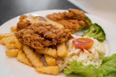 Kızarmış tavuk pirzolası, altın kırışık patates kızartması ve taze salata, marul, domates ve brokoli içeren iştah açıcı bir tabak..