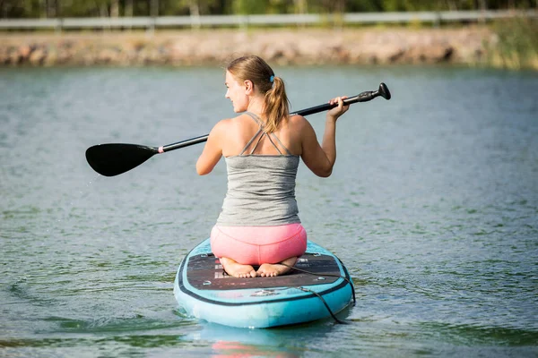 スーパーボード上の彼女の膝の上に立っている川に沿ってパドリングする若い運動女性 — ストック写真