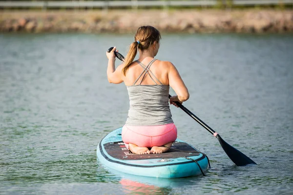 年轻的女运动员在河边划桨 双膝跪在跳板上 — 图库照片