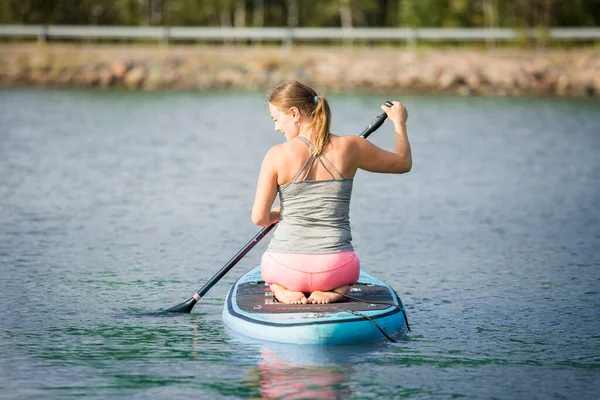 スーパーボード上の彼女の膝の上に立っている川に沿ってパドリングする若い運動女性 — ストック写真