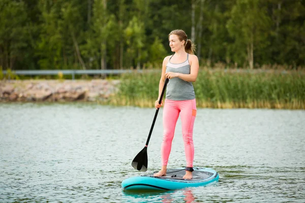 年轻的女运动员站在冲浪板上沿河划桨 — 图库照片