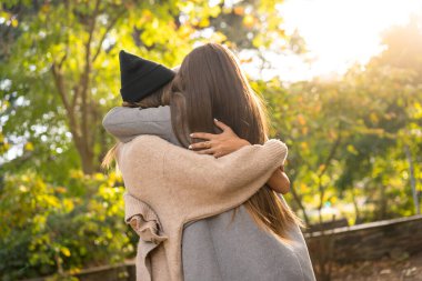 Sonbahar yaşam tarzı, kadın arkadaşları sonbaharda gün batımında parkta sarılıyorlar.