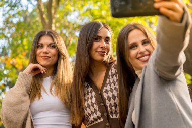Sonbaharda parkta gülümseyen kadın arkadaşlar kaygısızca selfie çekiyorlar, sonbahar yaşam tarzları.