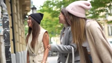 Sonbaharda şehirde alışveriş yapan arkadaşlar, gülümseyen ve tekliflere işaret eden mağaza camlarına bakarlar.