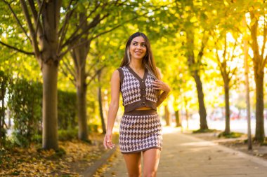 Sonbaharda beyaz esmer bir kadın şehirde sonbahar yaşam tarzı olan doğal bir parkta yürüyor.