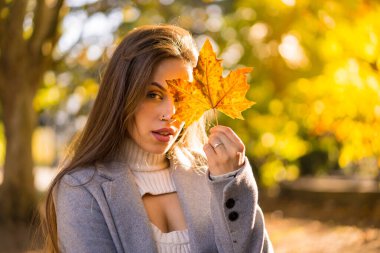 Gün batımında parkta sonbaharın tadını çıkaran güzel bir kadın ağaçtan bir yaprak gösteriyor.