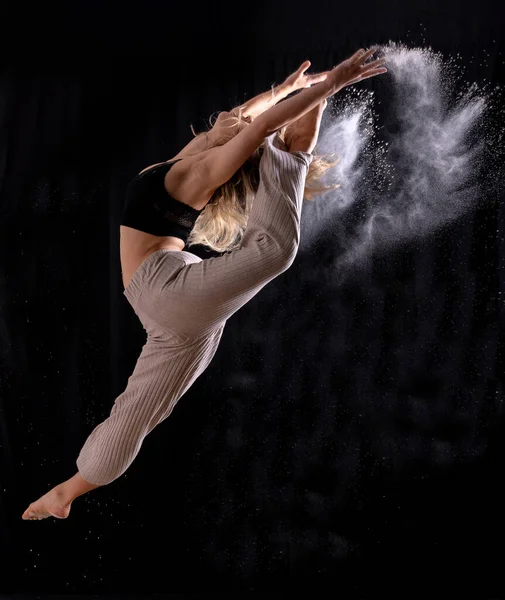 Young dancer performing a jump on a black background, ballet, freezing the image with dust or flour
