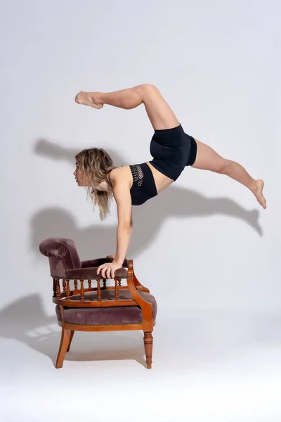 Young dancer on a white background, ballet, performing a jump with a sofa, studio shot, hard shadow