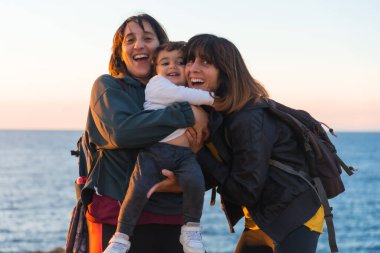 Anne ve çocuğun teyzesi gün batımında deniz kıyısında çocuğuna sarılıyordu.