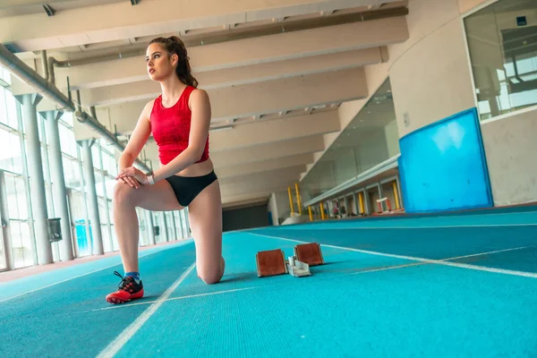 Indoor athletics, sprinter woman preparing and stretching before training