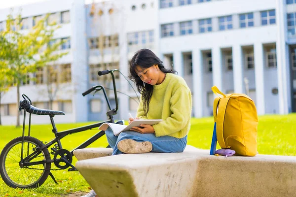 Asian art student sitting in college campus making a drawing in a notebook
