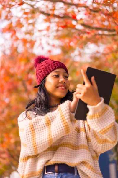 Asian girl walking in autumn with a tablet in her hand in a forest of red leaves, technology concept