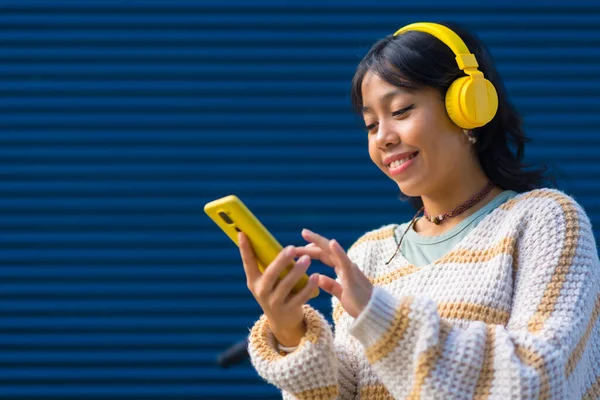 Ασιάτισσα Χαμογελαστή Ακούγοντας Μουσική Κίτρινα Ακουστικά Μπλε Πανεπιστημιακό Φόντο — Φωτογραφία Αρχείου